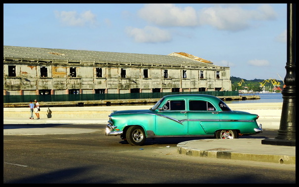 vintage green car driving on Havana's malecon near the ferry piers & warehouses